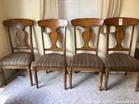 Front view of four wooden dining chairs with fabric seats, showing design and condition.