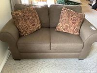 Front view of brown fabric love seat with two patterned pillows on the cushions.