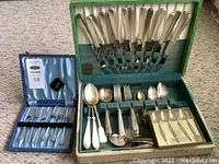 Full view of Tudor plate flatware including knives, forks, spoons and serving utensils in green flatware case along with additional boxed silver forks.