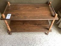 Full view of vintage wooden TV stand showing two shelves, turned legs and casters on carpet.