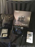 Camera, box, charger and carrying case displayed on black fabric.