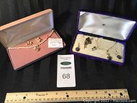 Wide view showing two sets of jewelry: one pearl floral necklace and earrings set in pink case, and a smaller set with stud earrings, brooch, and necklace with dark stone in purple case