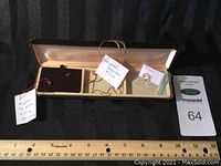 Box containing two small gold stud earrings with pink stones, a gold necklace, and gold hoop earrings with measurement ruler
