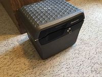 Closed black Sentry fire safe with a textured honeycomb pattern on the lid, sitting on carpet.