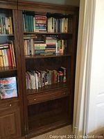 Full view of the wooden bookcase filled with books, showing the upper shelves, drawer, and bottom compartment
