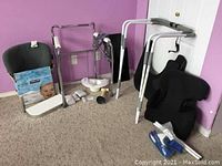 Photo showing a metal walker with padded handles, foldable bed rails, and two black ergonomic Obus back support cushions placed on the carpet.