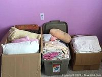Three containers filled with folded linens, pillows and blankets against a lavender wall