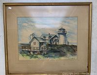 Framed pastel artwork showing lighthouse and buildings on rocky shore with muted blue and green tones.