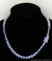 Full view of the necklace displayed on a black velvet bust, showing round and oval pale blue beads with the frog pendant on the side.