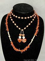 Front view of three coral-themed jewelry items on black velvet bust. Shows layered necklaces with coral beads and white beads plus heart earrings.