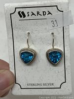 Front view of earrings on Sarda card showing triangular blue stones with sterling silver hooks and border detail.