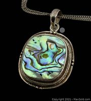 Close-up photo showing the pendant front with iridescent abalone shell pattern and detailed silver bezel.
