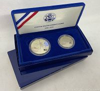 Open blue velvet box showing two United States proof coins inside protective capsules. Inner lid with US emblem and 'United States Liberty Coins 1886-1986'.