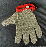 Full view of the chainmail safety glove laid flat showing the metal mesh and red fabric wrist strap.