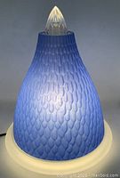 Blue textured glass lamp switched on showing the light glowing through the raised scale pattern