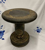 Front and side view of a carved wooden stool showing geometric carved designs on the round seat and cylindrical support, black finish with natural wood color in the carvings.