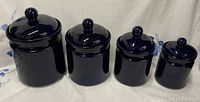 Four blue stoneware jars arranged in size order from largest to smallest, all with lids featuring round knob handles.