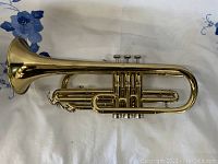 Side view of the brass trumpet showing its body and three mother of pearl valve buttons.