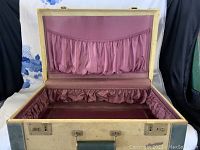 Open suitcase with purple satin lining and gathered pockets on lid and base.