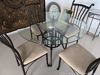 Glass dining table with four metal frame chairs around it, beige cushioned seats visible, slight scratches noted on glass.