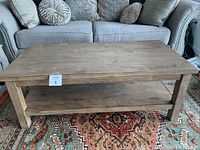 Front view of the rectangular wooden coffee table with natural wood finish on a patterned rug in front of a gray sofa, showing the water stain on the top surface.