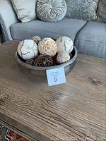 Silver bowl on wooden table filled with decorative balls of various textures and colors