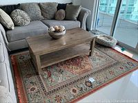 Rug displayed under wooden coffee table with sectional couch around.