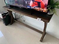 Front view of the dark brown wooden stand supporting a television and a plant.