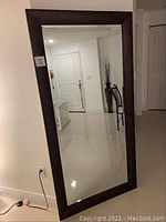 Standing rectangular vanity mirror with a broad dark cherry oak wooden frame, shown angled against a wall in a clean interior room.