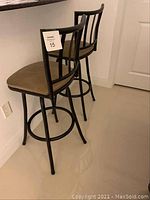 Two black metal frame bar stools with brown cushioned seats and vertical back support bars, viewed from behind, positioned at a counter.