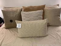 Front view of all 5 decorative pillows arranged on a striped beige bedspread, showing various textures and neutral tones.