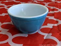 Blue Pyrex mixing bowl showing side profile and partial interior, placed on a red cloth with white pattern.