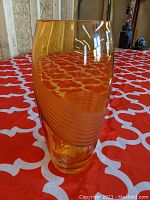 View of amber glass vase highlighting the polished rim and spiral etched design swirling around the ovoid body