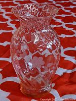 Clear glass vase with visible floral and wave etched designs from front angle on patterned red background.