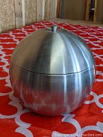Photo showing the closed apple-shaped stainless steel ice bucket with lid, placed on a patterned red and white cloth.