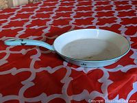 Side view of light blue handled cast iron skillet with white enameled interior and tulip motif on handle