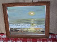Full view of the framed oil painting showing the beach moonrise scene with wooden frame and matte border.