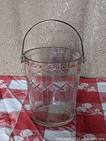 Front view of clear depression glass ice bucket showing vertical etched stripes and diamond band cut design with attached metal handle.