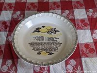 Top view of the off-white ceramic pie plate showing the printed Lemon Meringue recipe with black and yellow lemon illustrations and a scalloped black-bordered rim.