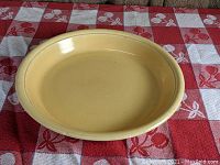 Front angled view showing color, shape and detailed rim of the yellow pie plate on a red and white checkered cloth with cherries.