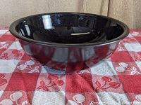 Side view of large black glossy glass mixing bowl showing shape and rim detail.