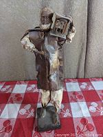 Front view of folk art sculpture depicting a poultry farmer holding a birdcage with a bird inside, made of sculpted paper and mounted on a square base.