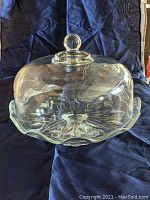 Glass cake stand with clear dome lid and ball handle photographed against dark fabric background from side angle