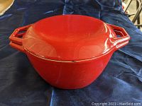 Side angle front view of red cast iron Dutch oven with lid, showing minor chip on the enamel at the edge.