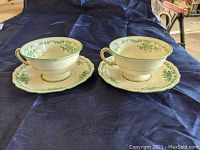 Two teacups and saucers displayed side by side on dark blue fabric showing their profile view.