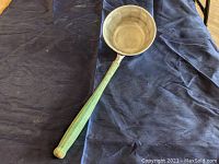 Top view showing the rounded aluminum scoop and long green wooden handle of the dipper placed on a dark surface.