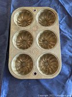 Top view of the muffin pan showing 6 cup compartments with swirl pattern and the Ekco brand mark embossed on the pan.