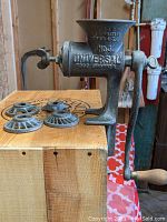 Wide angle photo showing antique Universal No3 Food Grinder with 4 accompanying grinding disks on wooden surface.