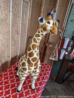 Front angle of the large stuffed giraffe plush on a red tablecloth with white interlocking pattern.
