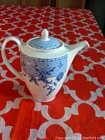 Front view of coffee pot showing curved spout, handle, and detailed blue floral pattern on white porcelain.